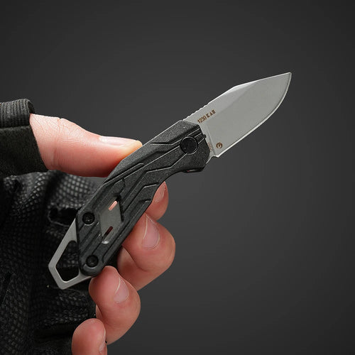 Hand holding a black folding knife against a dark background